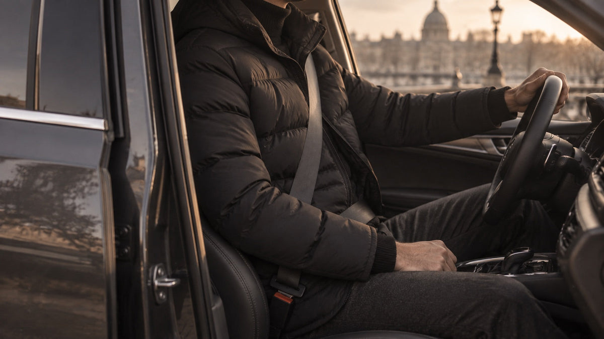 Un homme au volant en manteau court matelasse, ceinture de securite bouclee par-dessus Image